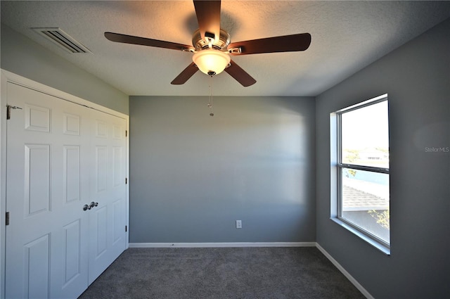 unfurnished bedroom with ceiling fan, a textured ceiling, and dark carpet