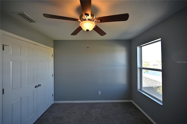 unfurnished bedroom with ceiling fan, a textured ceiling, and dark carpet