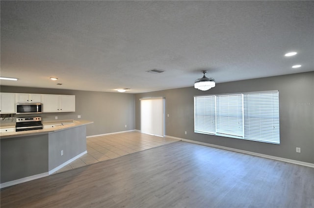 kitchen featuring a textured ceiling, light hardwood / wood-style flooring, stainless steel appliances, and white cabinets