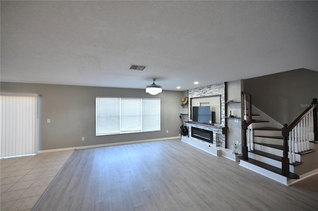 unfurnished living room featuring a stone fireplace, light hardwood / wood-style flooring, and a textured ceiling