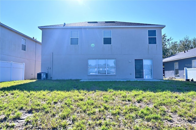 rear view of property with central air condition unit and a lawn