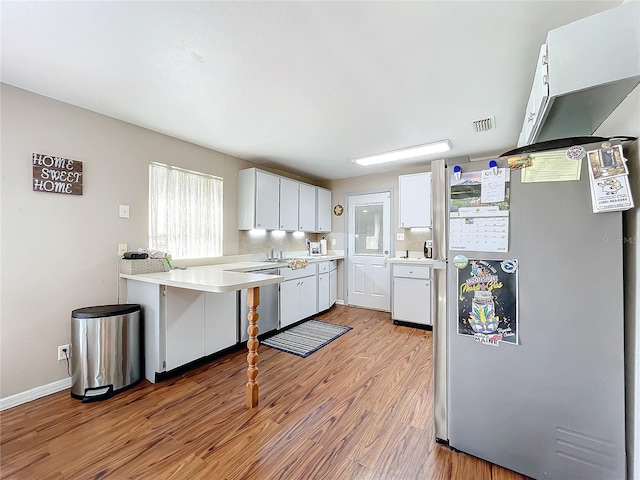 kitchen with sink, light hardwood / wood-style flooring, stainless steel fridge, white cabinets, and kitchen peninsula