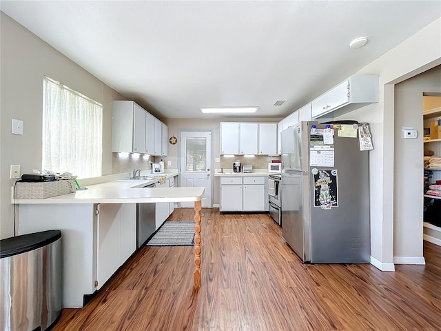 kitchen featuring hardwood / wood-style floors, backsplash, stainless steel appliances, white cabinets, and kitchen peninsula