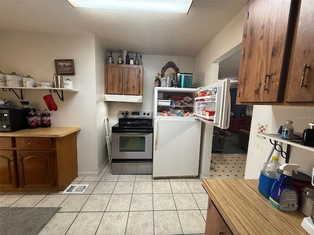 kitchen featuring refrigerator, light tile patterned floors, a textured ceiling, and stainless steel range with electric stovetop