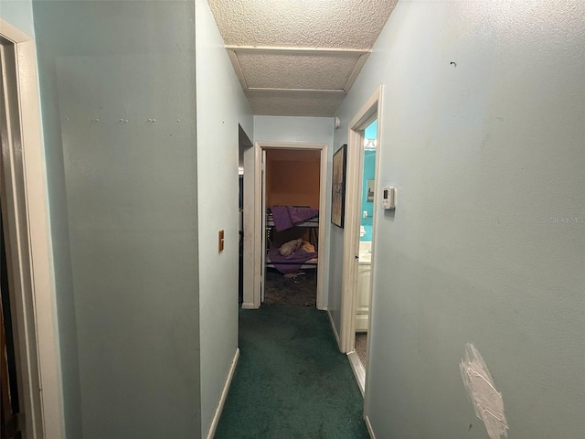 hall featuring a textured ceiling and dark colored carpet