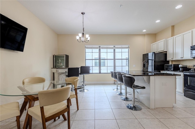 kitchen with a breakfast bar, decorative light fixtures, an island with sink, white cabinetry, and black appliances