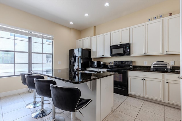 kitchen featuring sink, a breakfast bar area, an island with sink, dark stone counters, and black appliances