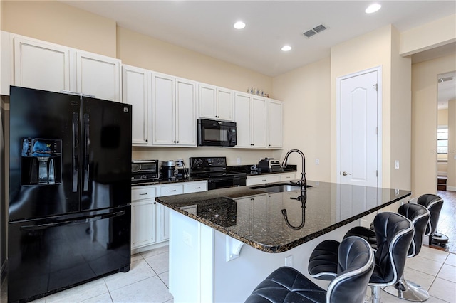 kitchen featuring sink, white cabinetry, a center island with sink, dark stone counters, and black appliances