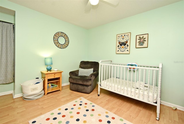 bedroom with a crib, hardwood / wood-style floors, and ceiling fan