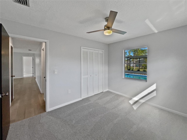 unfurnished bedroom featuring ceiling fan, carpet floors, a closet, and a textured ceiling