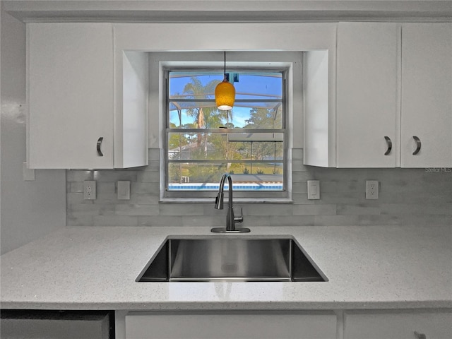 kitchen with sink, light stone counters, white cabinets, pendant lighting, and backsplash