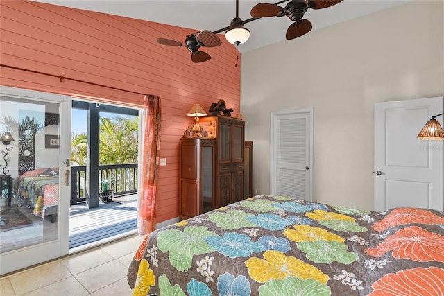 bedroom with light tile patterned flooring, a towering ceiling, wooden walls, access to outside, and ceiling fan