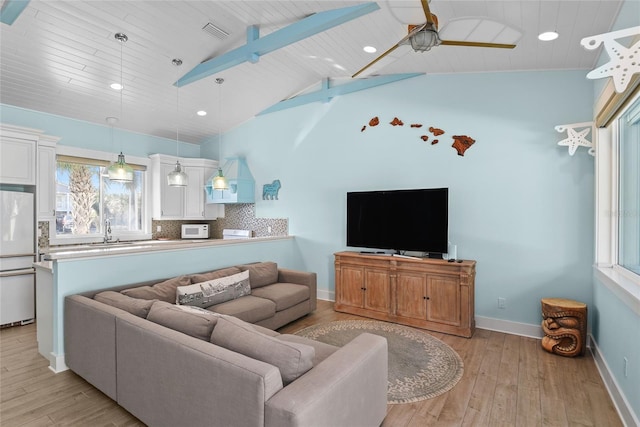 living room featuring ceiling fan, sink, light hardwood / wood-style flooring, and vaulted ceiling with beams