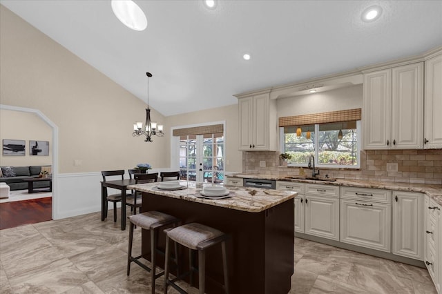 kitchen with vaulted ceiling, decorative light fixtures, sink, a center island, and light stone counters