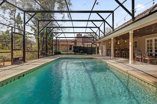 view of swimming pool with ceiling fan, a patio area, glass enclosure, and a bar