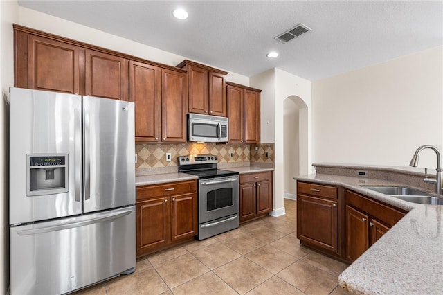 kitchen featuring sink, decorative backsplash, light tile patterned floors, stainless steel appliances, and light stone countertops