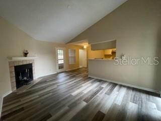 unfurnished living room featuring a tiled fireplace, vaulted ceiling, and dark wood-type flooring