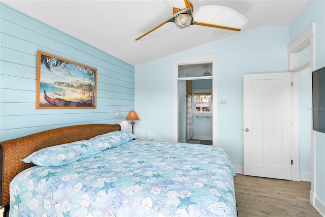 bedroom with vaulted ceiling, ceiling fan, wooden walls, and light hardwood / wood-style floors