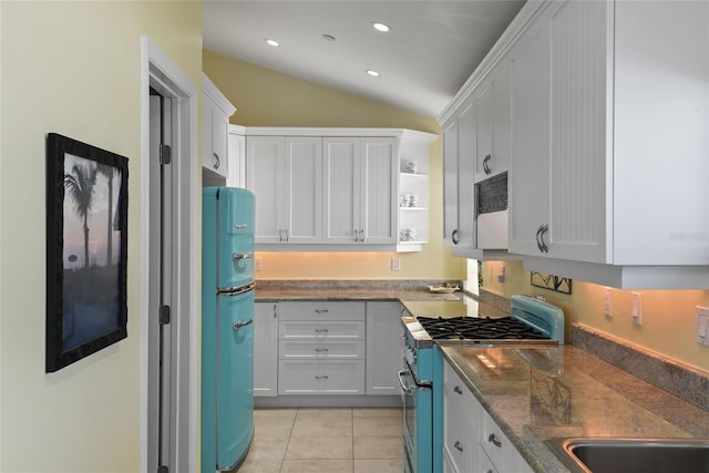 kitchen with stainless steel gas range, refrigerator, vaulted ceiling, light tile patterned floors, and white cabinets