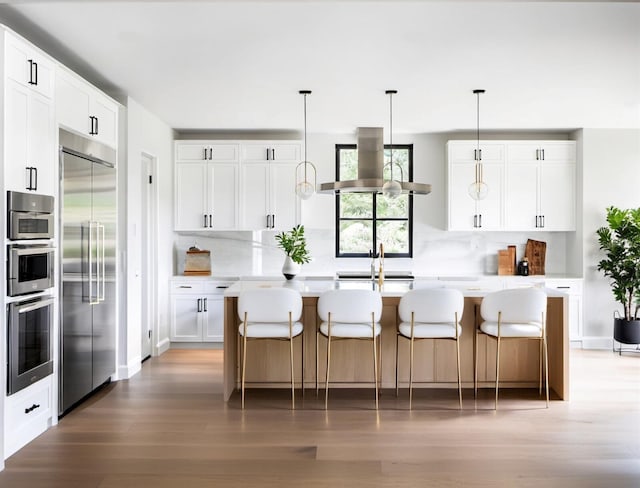 kitchen featuring stainless steel appliances, sink, an island with sink, and white cabinets