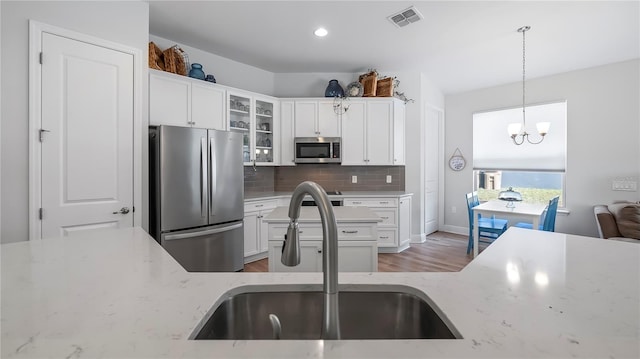 kitchen with decorative light fixtures, tasteful backsplash, sink, stainless steel appliances, and light stone countertops