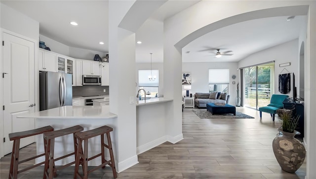 kitchen with white cabinets, backsplash, kitchen peninsula, stainless steel appliances, and light hardwood / wood-style flooring