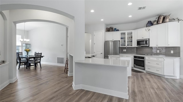 kitchen featuring pendant lighting, light hardwood / wood-style flooring, backsplash, stainless steel appliances, and white cabinets