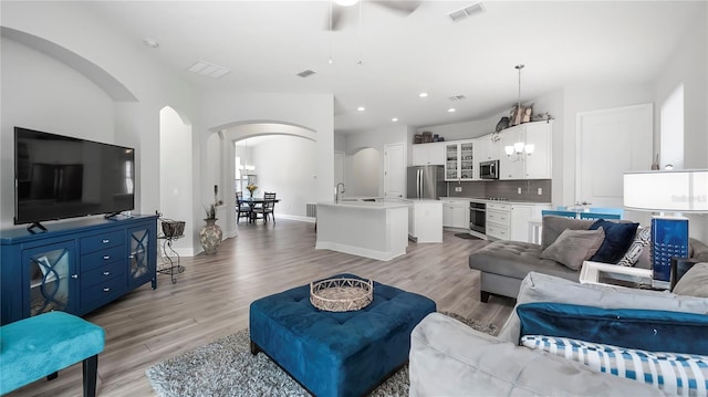 living room with sink, ceiling fan with notable chandelier, and light wood-type flooring