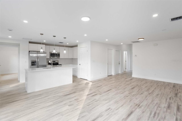 kitchen featuring sink, hanging light fixtures, light hardwood / wood-style floors, stainless steel appliances, and a center island with sink