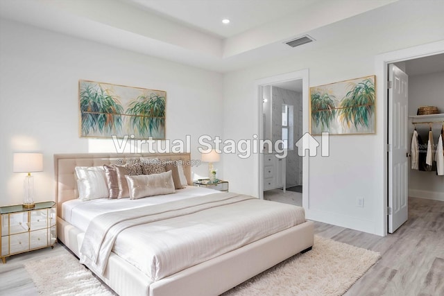 bedroom with a raised ceiling, ensuite bath, and light hardwood / wood-style floors