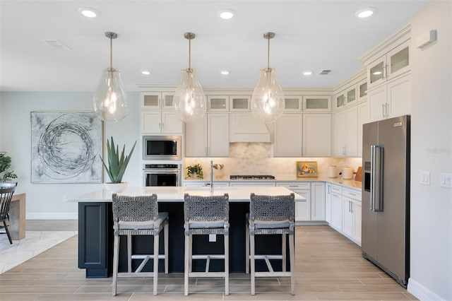 kitchen with stainless steel appliances, an island with sink, hanging light fixtures, and decorative backsplash