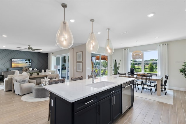 kitchen with decorative light fixtures, an island with sink, sink, stainless steel dishwasher, and ceiling fan