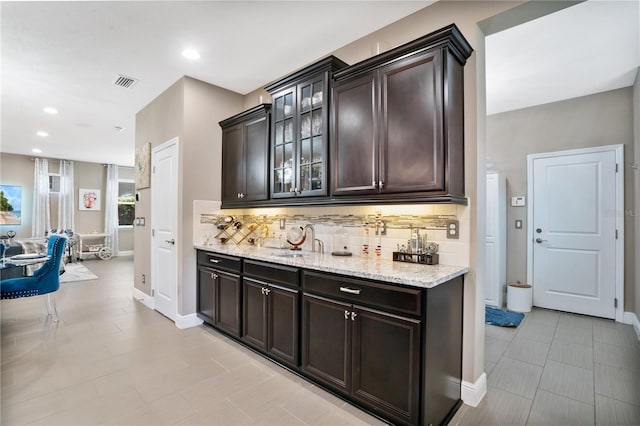 bar featuring dark brown cabinets, sink, and backsplash