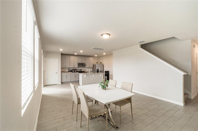 dining room with light wood-style flooring, visible vents, stairway, and baseboards