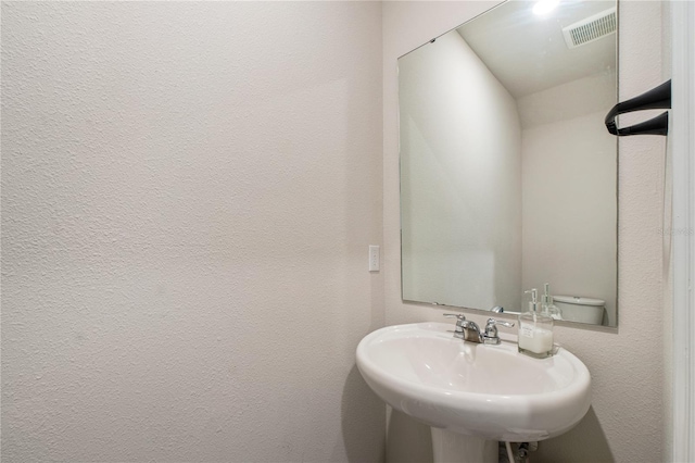 bathroom with a textured wall, a sink, and visible vents