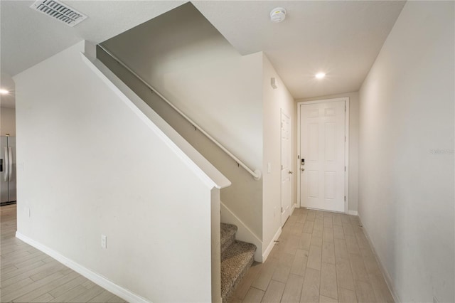 hall with light wood-type flooring, baseboards, stairs, and visible vents