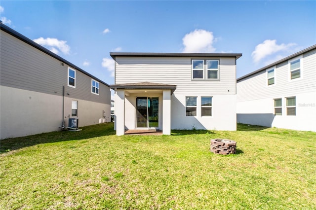 rear view of house with an outdoor fire pit, central AC, and a yard