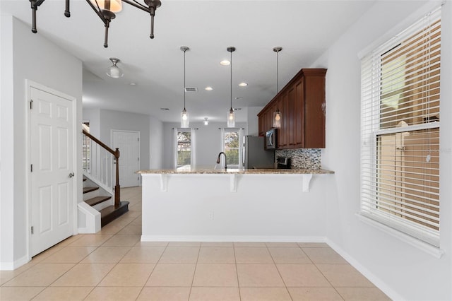 kitchen featuring light tile patterned floors, appliances with stainless steel finishes, decorative backsplash, decorative light fixtures, and kitchen peninsula