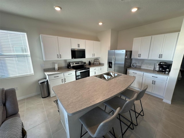 kitchen featuring sink, a kitchen breakfast bar, stainless steel appliances, a kitchen island with sink, and white cabinets