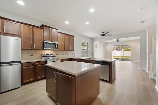 kitchen featuring sink, appliances with stainless steel finishes, a kitchen island, kitchen peninsula, and light wood-type flooring