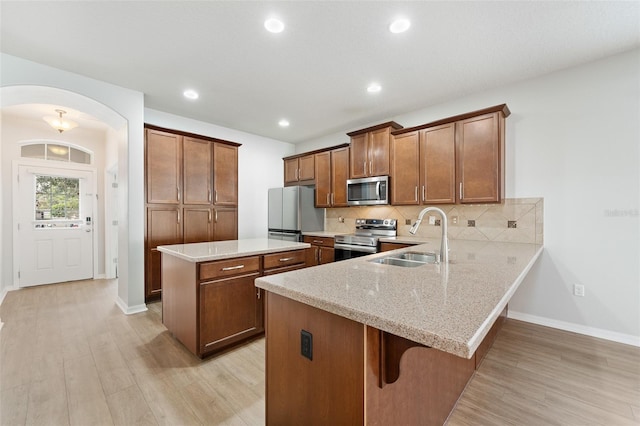 kitchen featuring sink, decorative backsplash, light hardwood / wood-style floors, kitchen peninsula, and stainless steel appliances