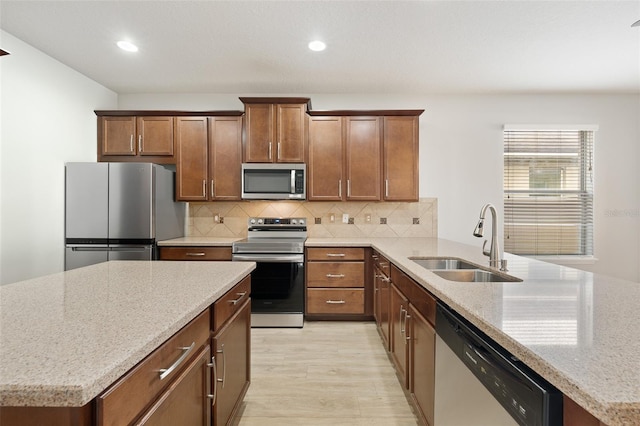 kitchen featuring sink, decorative backsplash, light hardwood / wood-style floors, stainless steel appliances, and light stone countertops