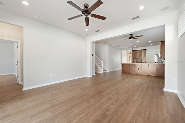 unfurnished living room with ceiling fan, sink, and light wood-type flooring