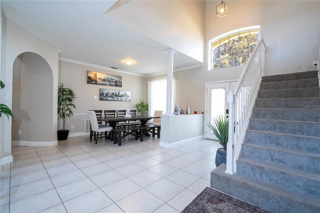 tiled foyer entrance featuring ornamental molding, decorative columns, and a high ceiling