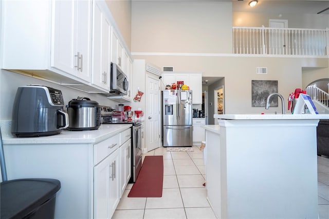 kitchen featuring white cabinetry, a high ceiling, a kitchen island with sink, light tile patterned floors, and stainless steel appliances