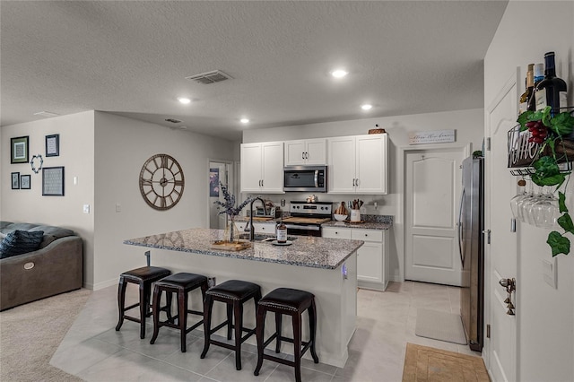 kitchen featuring light tile patterned flooring, appliances with stainless steel finishes, a breakfast bar, white cabinets, and a center island with sink