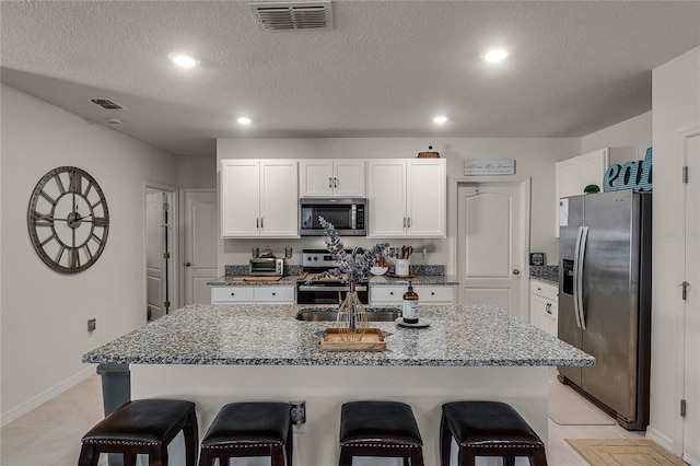 kitchen featuring white cabinets, stainless steel appliances, a kitchen island with sink, and light tile patterned floors