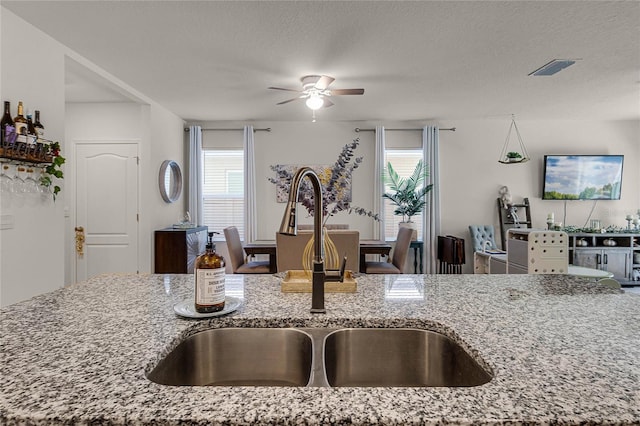 kitchen featuring light stone counters, a healthy amount of sunlight, sink, and a textured ceiling