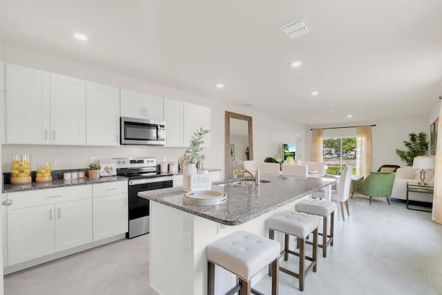 kitchen with sink, a breakfast bar area, stainless steel appliances, an island with sink, and white cabinets