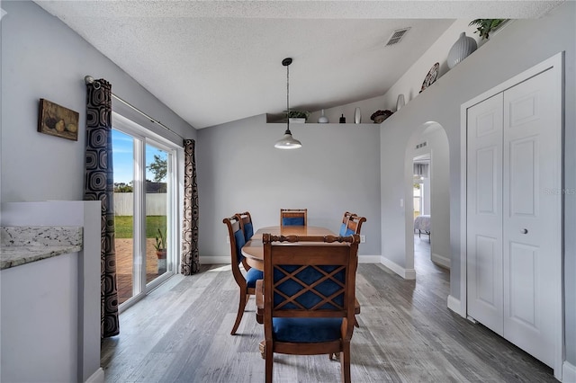 dining room featuring vaulted ceiling, arched walkways, visible vents, and light wood-type flooring